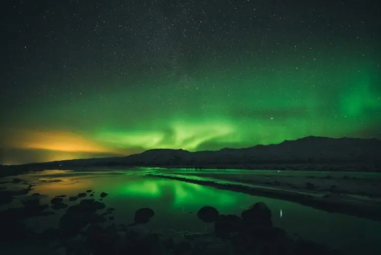Green Northern Lights illuminating the night sky above a mountain, seen from a boat.