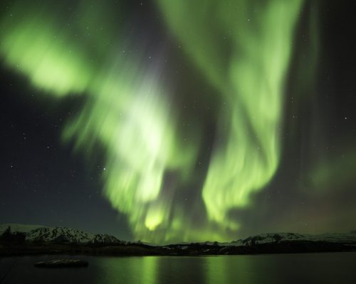 Green Northern Lights illuminating the night sky above a mountain, seen from a boat.